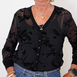 Casual chic outfit: woman in a black mesh cardigan and tank set with blue jeans and a maroon purse, standing against white background.