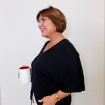 Woman in a black outfit holding a white mug with a red interior against a plain background