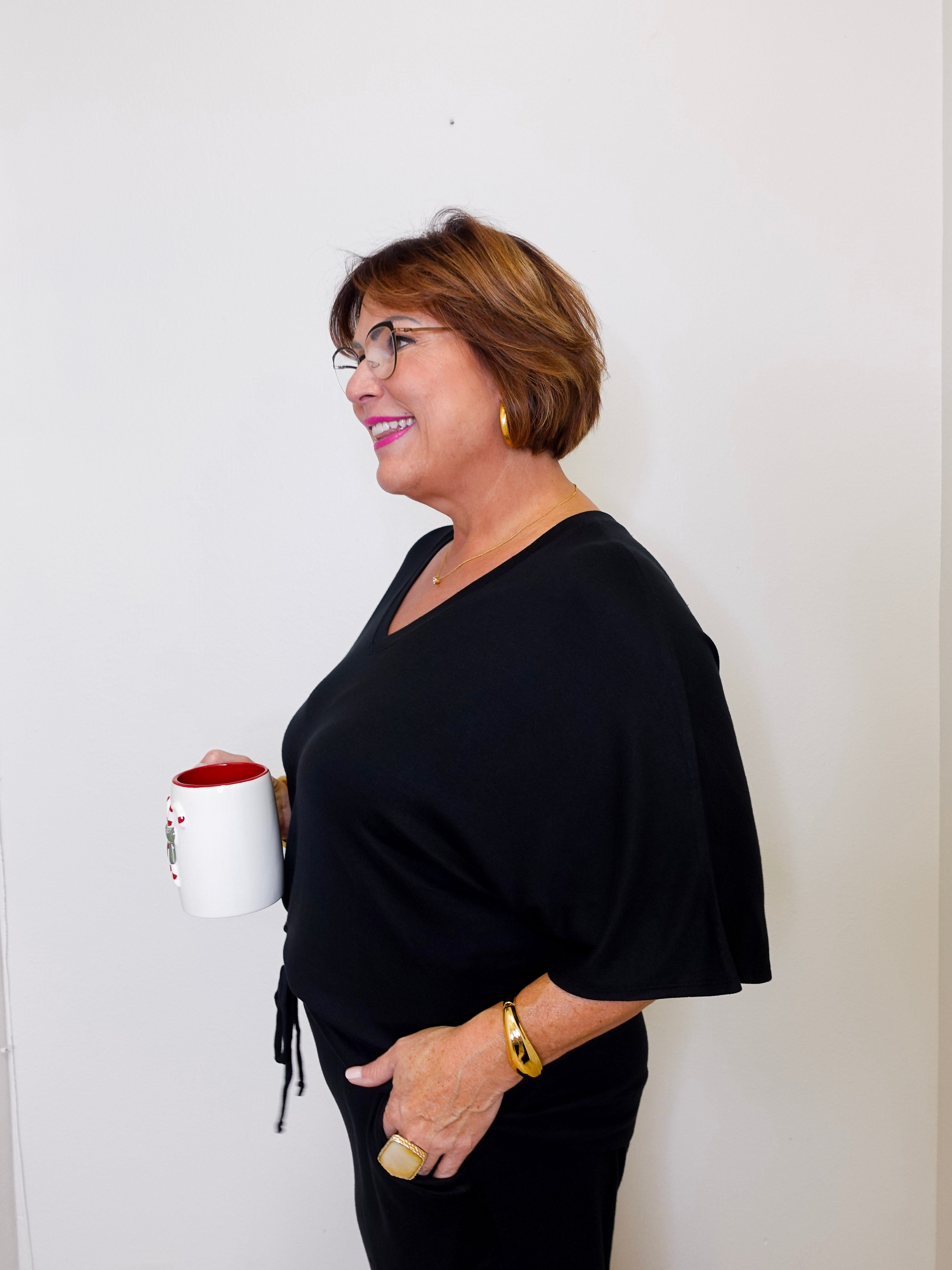 Woman in a black outfit holding a white mug with a red interior against a plain background
