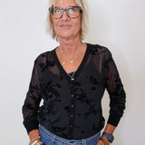 Model wearing a black mesh cardigan and tank set, blue jeans, and holding a maroon purse against a white backdrop.