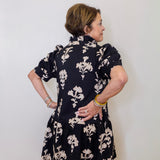 Woman wearing a black floral dress against a white wall