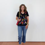 Woman wearing a black floral top and blue jeans against a white wall.