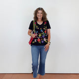 Woman wearing a black floral top and blue jeans against a white wall.