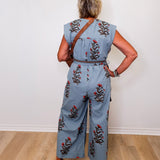 Person wearing a denim jumpsuit with floral embroidery standing against a white wall.