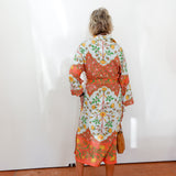 Woman wearing a colorful floral dress standing against a white wall.