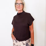 Woman wearing a brown top and floral pants against a white background