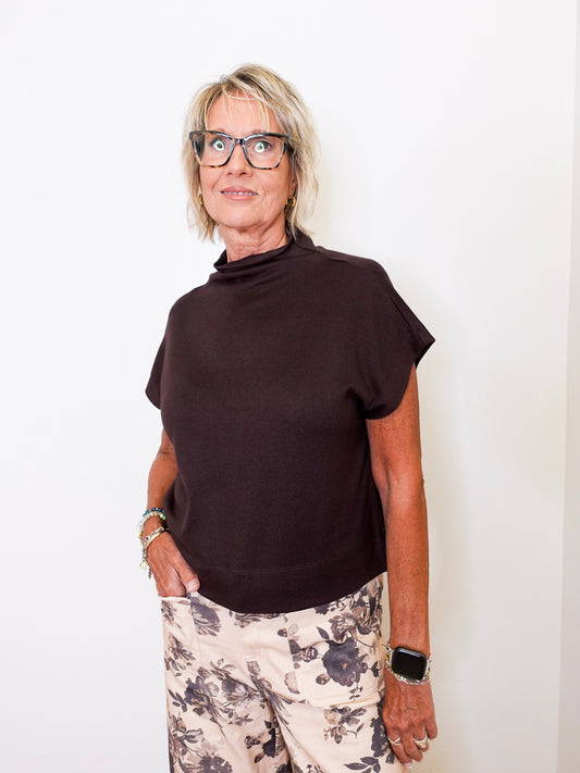 Woman wearing a brown top and floral pants against a white background