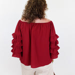 Person wearing a red off-shoulder blouse with ruffled sleeves on a white background