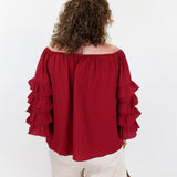 Person wearing a red off-shoulder blouse with ruffled sleeves on a white background