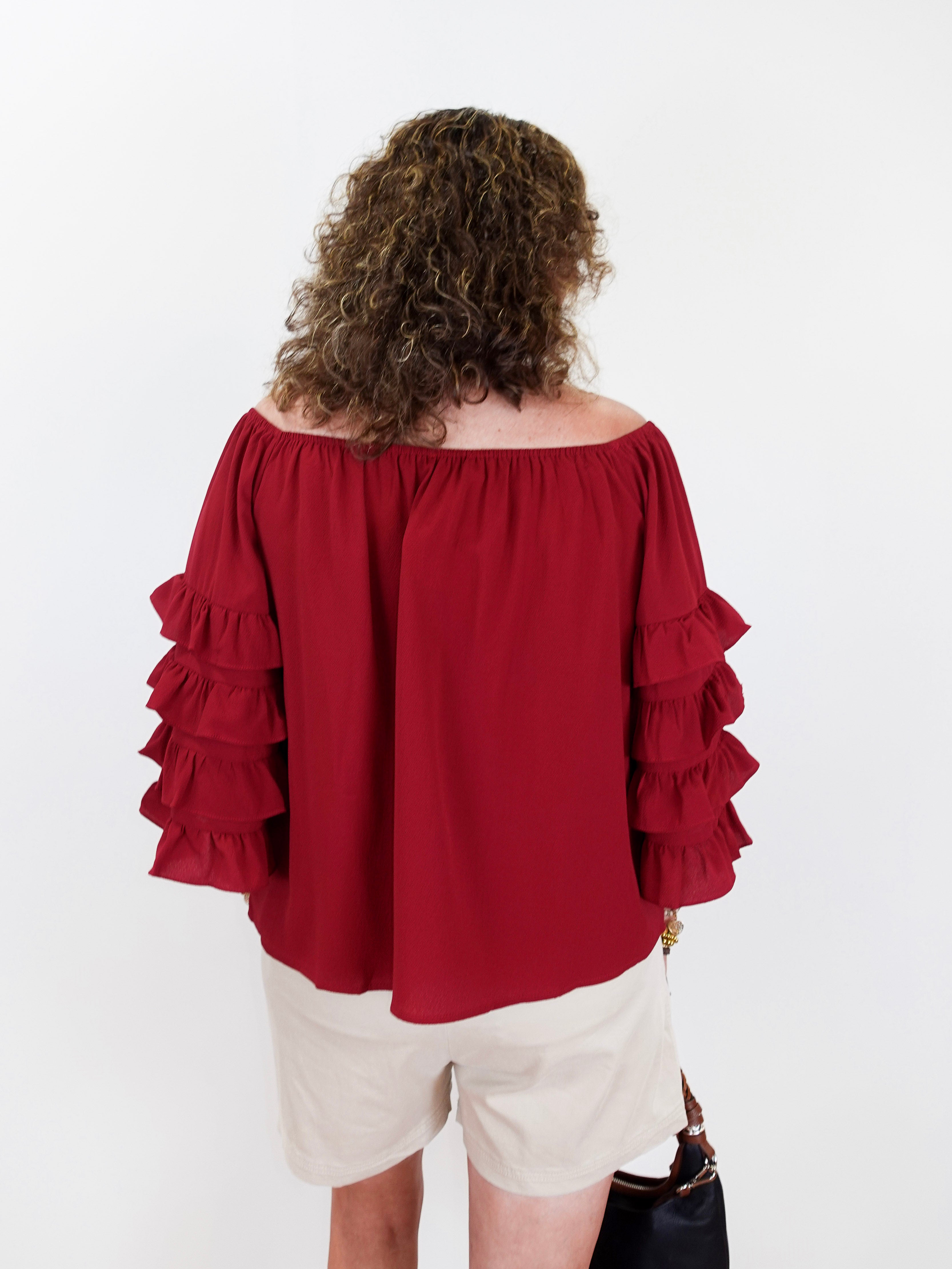 Person wearing a red off-shoulder blouse with ruffled sleeves on a white background
