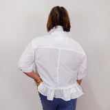 Person wearing a white blouse with ruffled details and blue jeans against a plain background