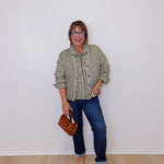 Woman wearing a patterned shirt and jeans against a white wall
