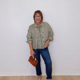 Woman wearing a patterned shirt and jeans against a white wall