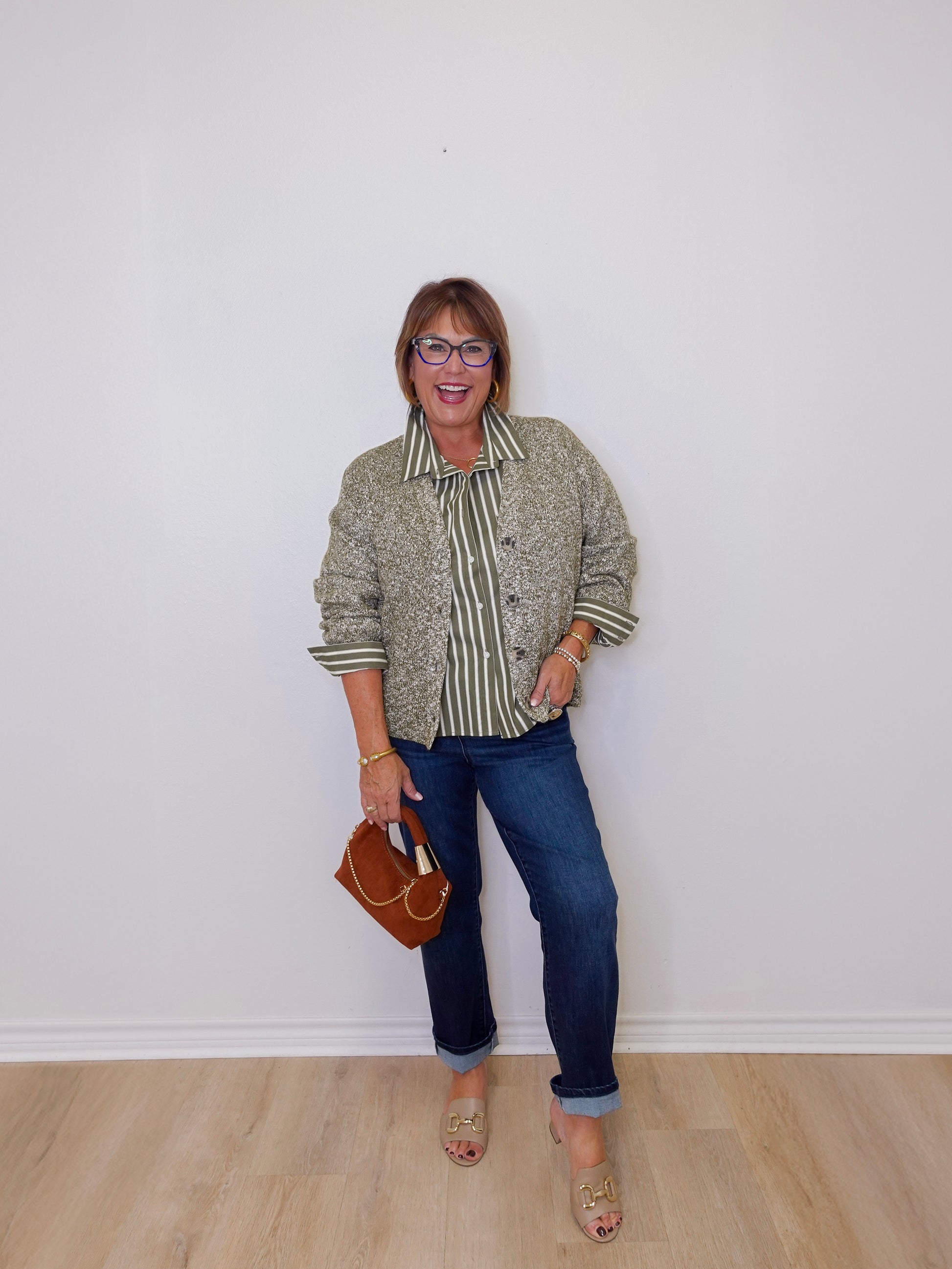 Woman wearing a patterned shirt and jeans against a white wall