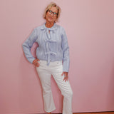 Woman wearing a light blue patterned blouse and white pants against a pink wall.