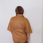 Person wearing a brown jacket against a white wall