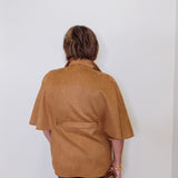 Person wearing a brown jacket against a white wall