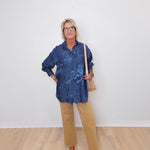 Person wearing a blue floral shirt and beige pants against a white wall.
