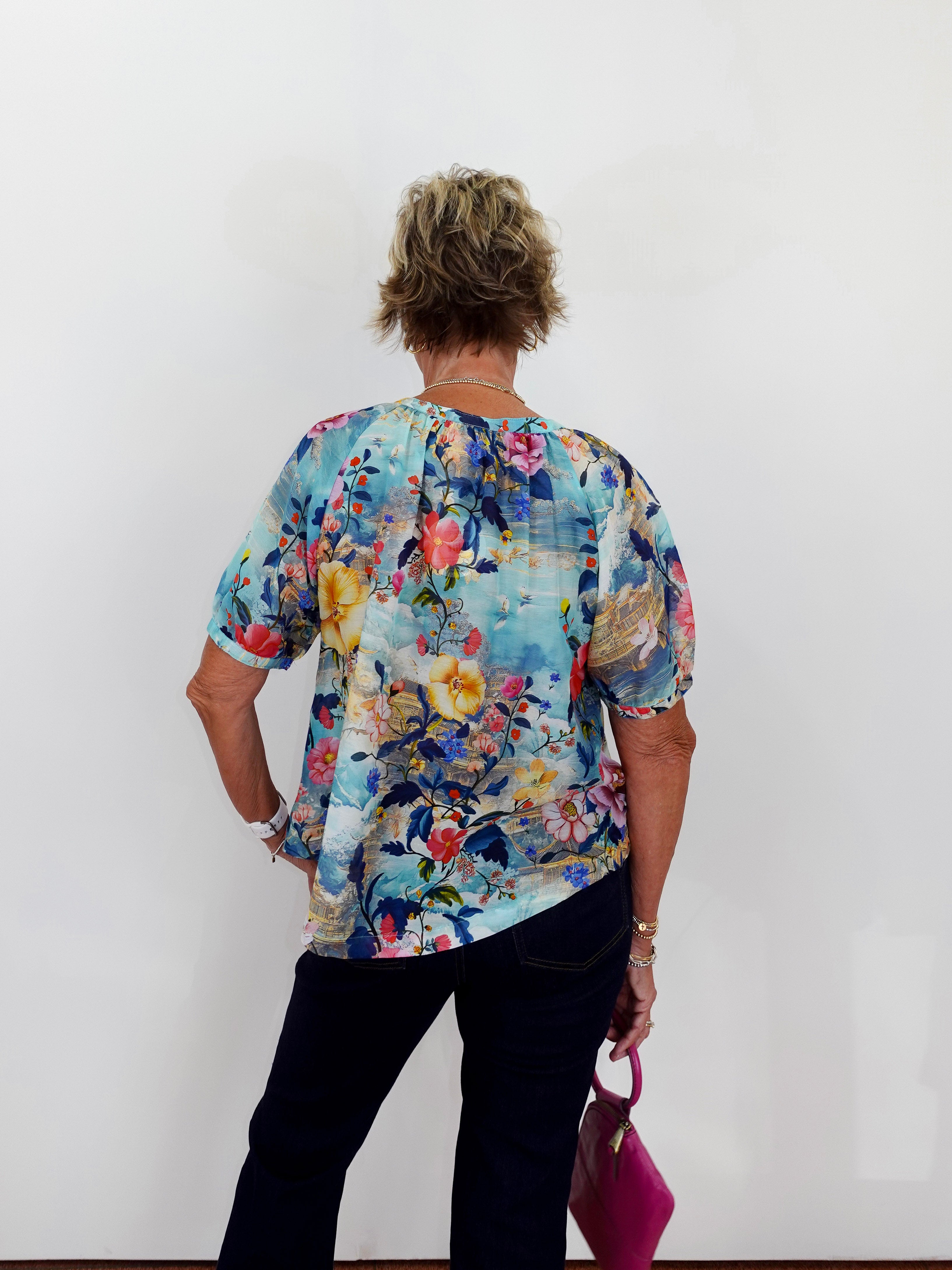 Person wearing a colorful floral blouse against a white wall