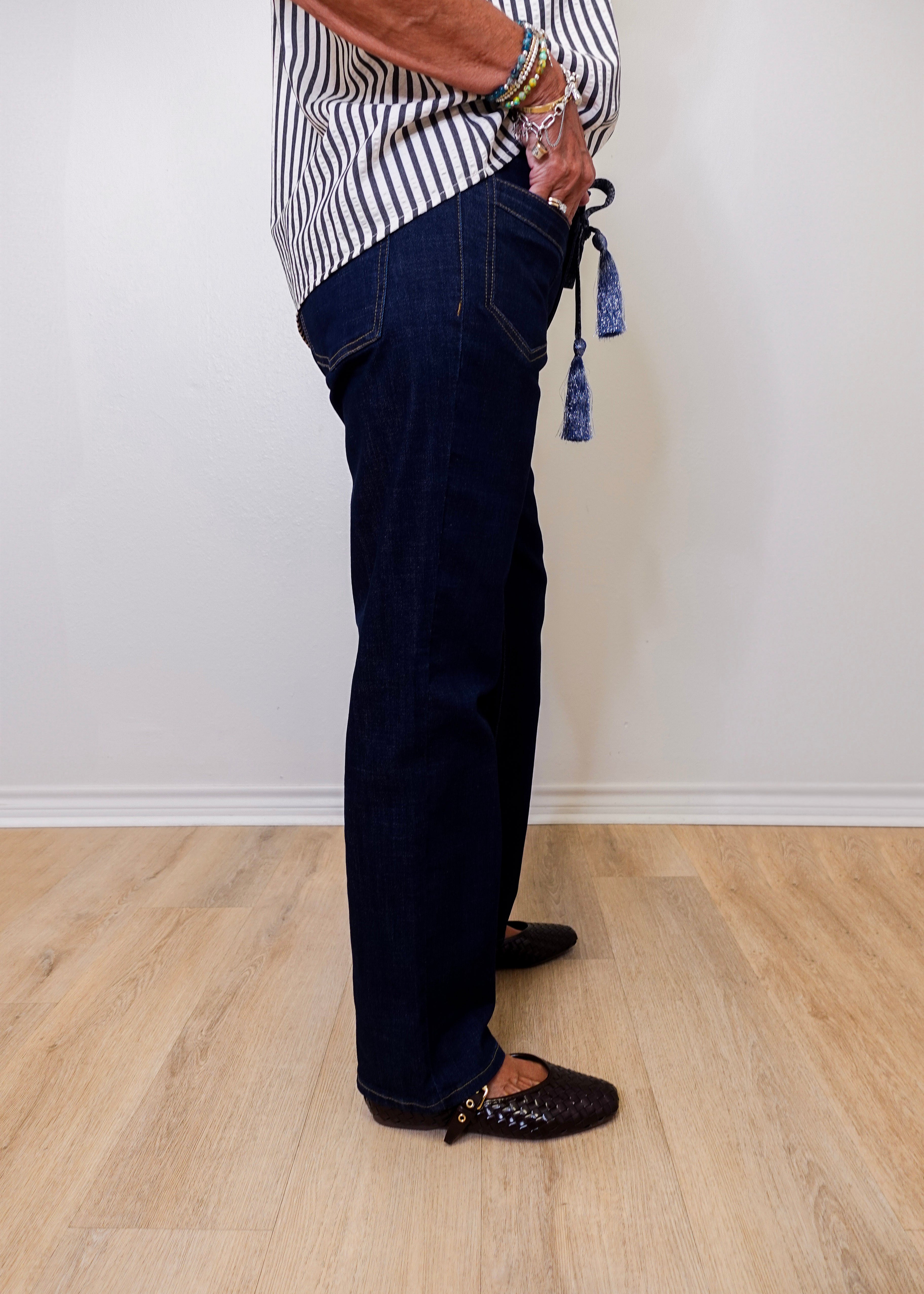 Person wearing dark blue jeans and a striped shirt on a light wooden floor.