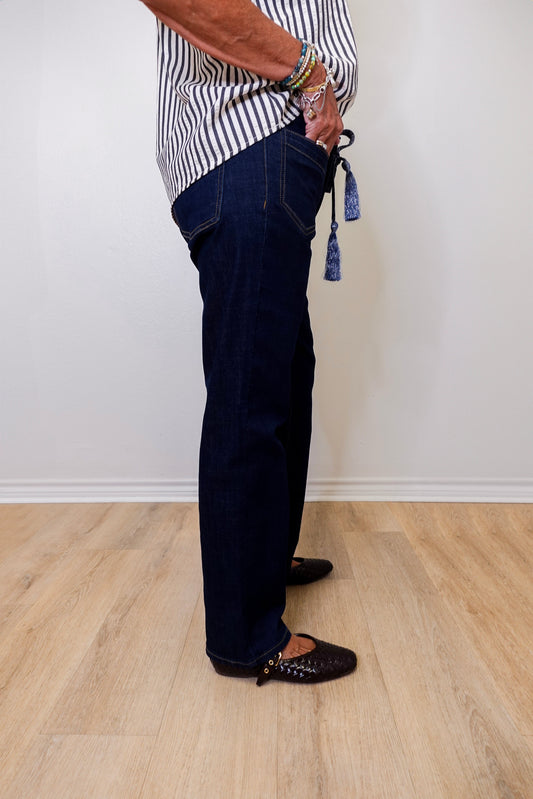 Person wearing dark blue jeans and a striped shirt on a light wooden floor.