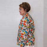 Woman wearing a colorful patterned jacket against a white wall