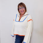Woman wearing a white sweater with colorful accents against a plain background