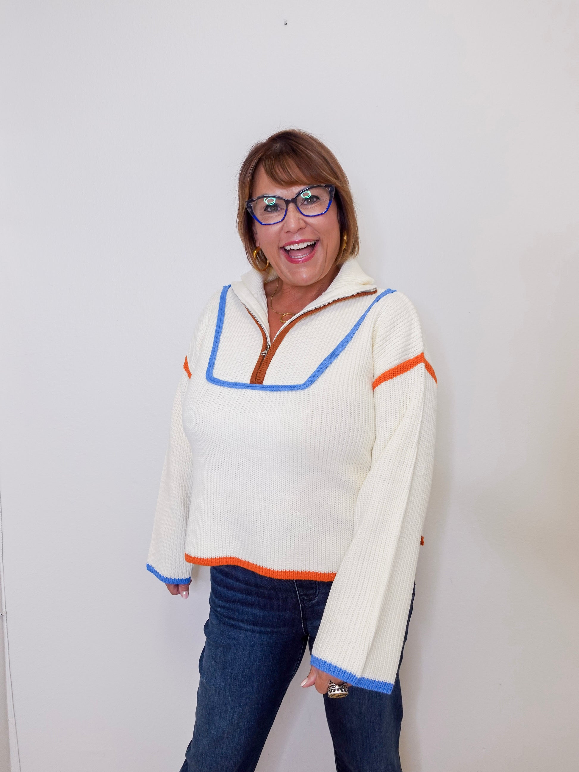 Woman wearing a white sweater with colorful accents against a plain background