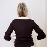 Person wearing a black sweater with a white collar against a plain background