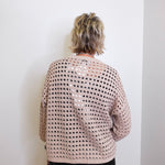 Person wearing a beige and black patterned sweater against a white wall