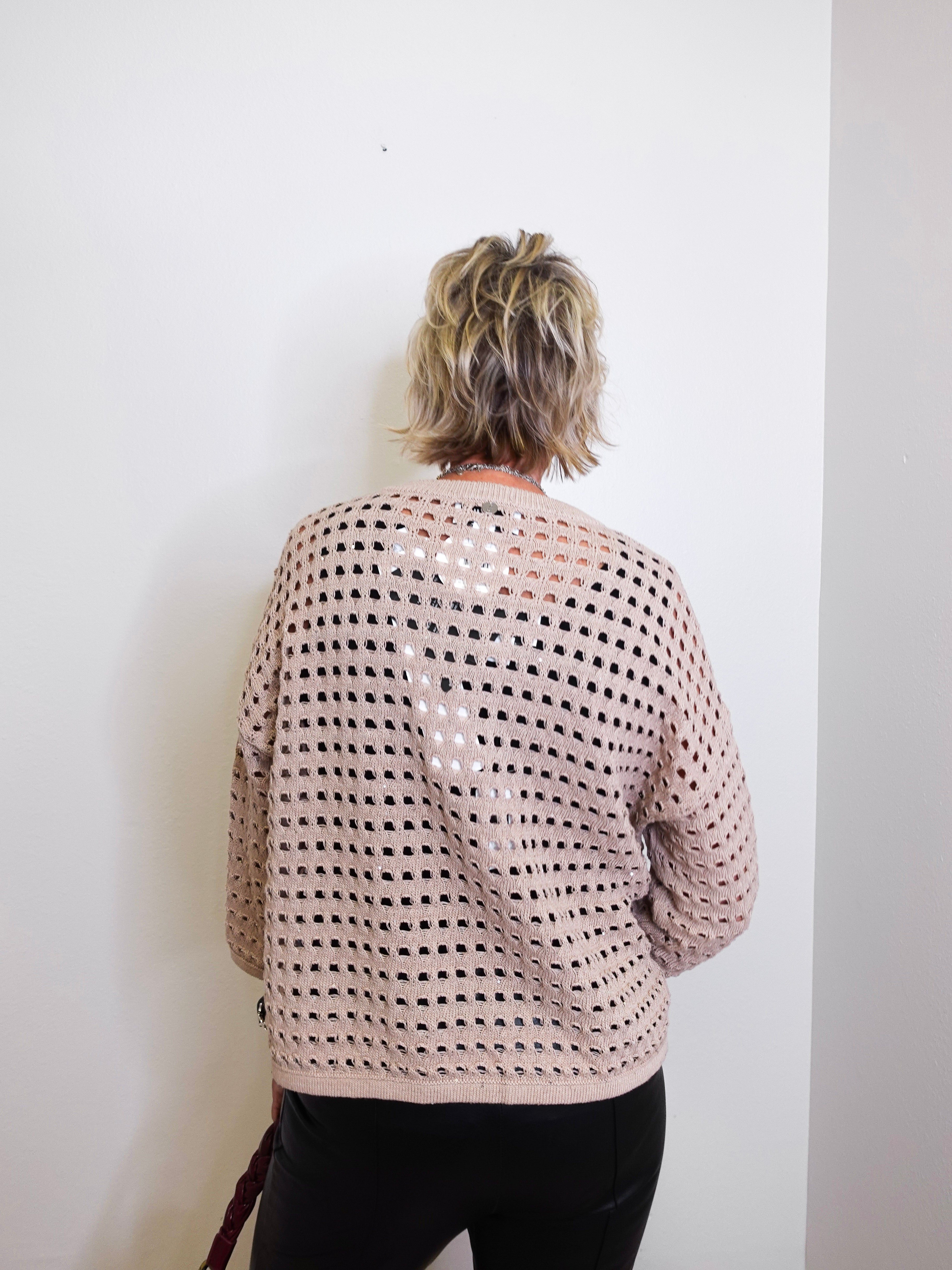 Person wearing a beige and black patterned sweater against a white wall