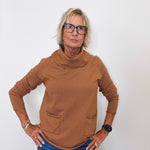 Stylish fall look: woman wearing a tan cowl neck sweater with denim jeans against white backdrop.