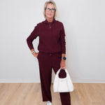 Woman wearing a burgundy outfit with a white handbag against a plain background