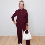 Woman wearing a burgundy outfit with a white handbag against a plain background