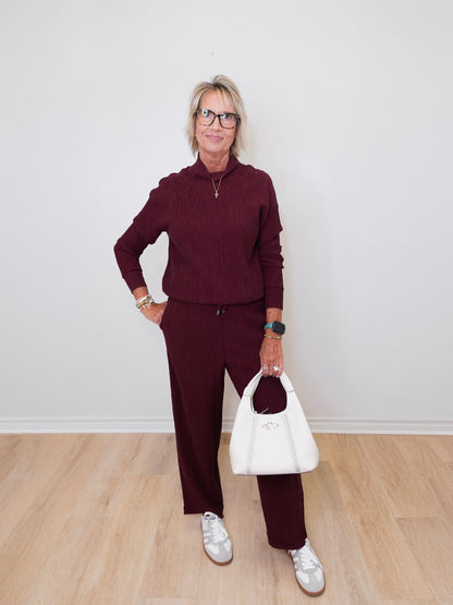 Woman wearing a burgundy outfit with a white handbag against a plain background