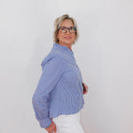 Woman wearing a blue checkered blouse and white pants against a plain background