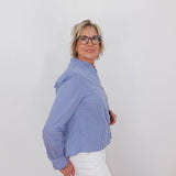 Woman wearing a blue checkered blouse and white pants against a plain background