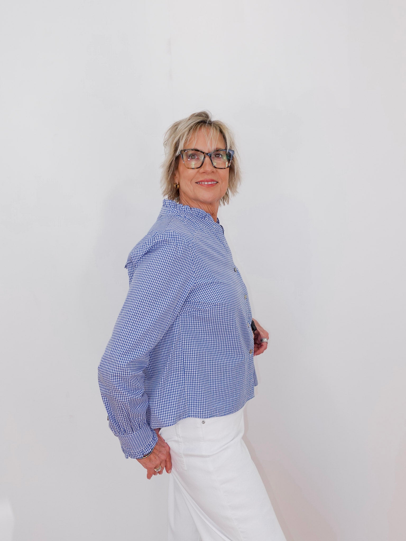 Woman wearing a blue checkered blouse and white pants against a plain background