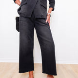 Person wearing a black outfit with wide-leg pants and loafers on a light wooden floor.