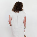 Person wearing a white dress standing against a plain background