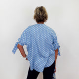 Person wearing a blue polka dot shirt with tied sleeves against a white background