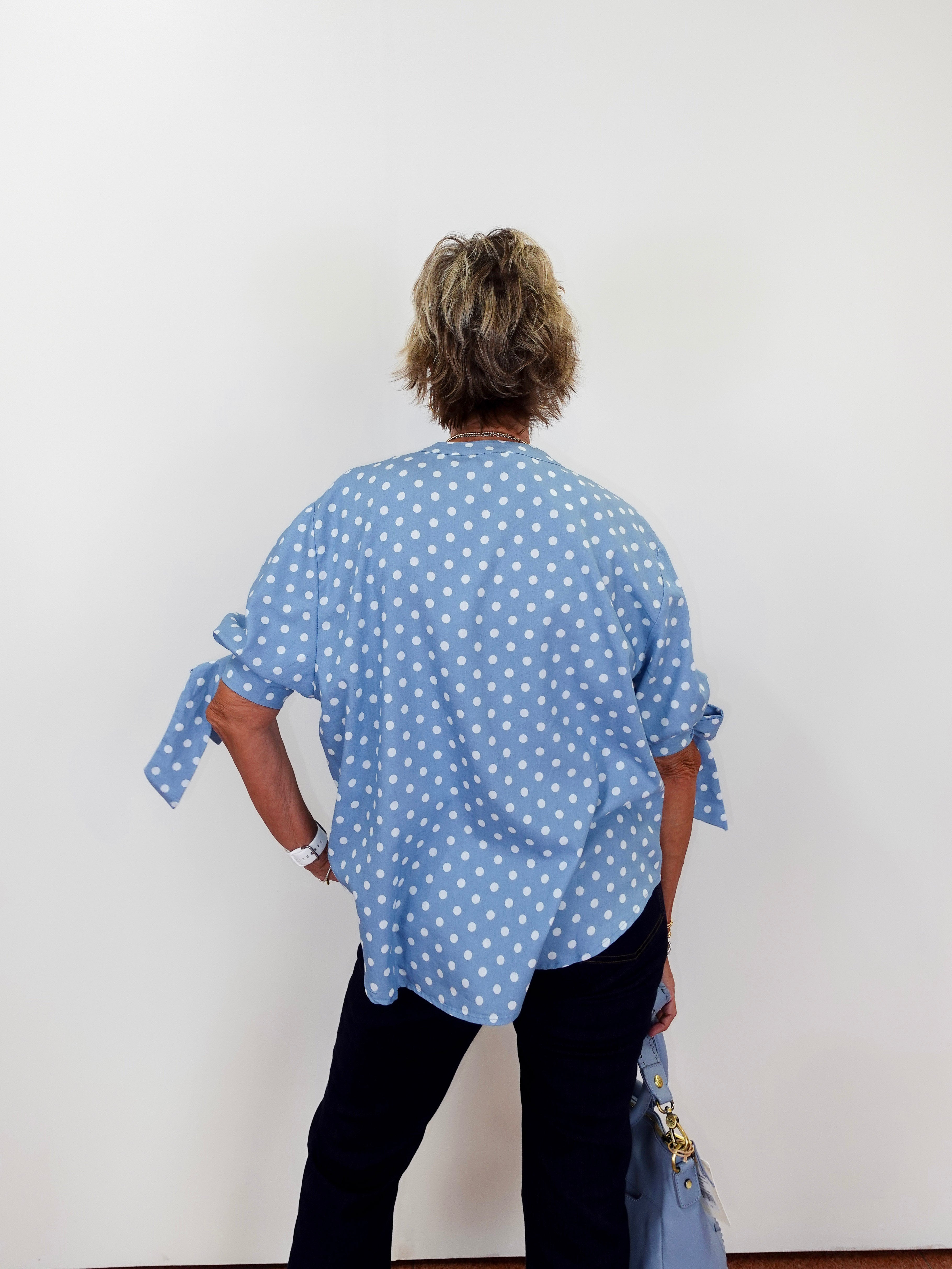 Person wearing a blue polka dot shirt with tied sleeves against a white background