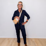 Person wearing a denim outfit with a beige bag against a white wall.