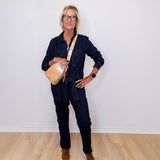 Person wearing a denim outfit with a beige bag against a white wall.