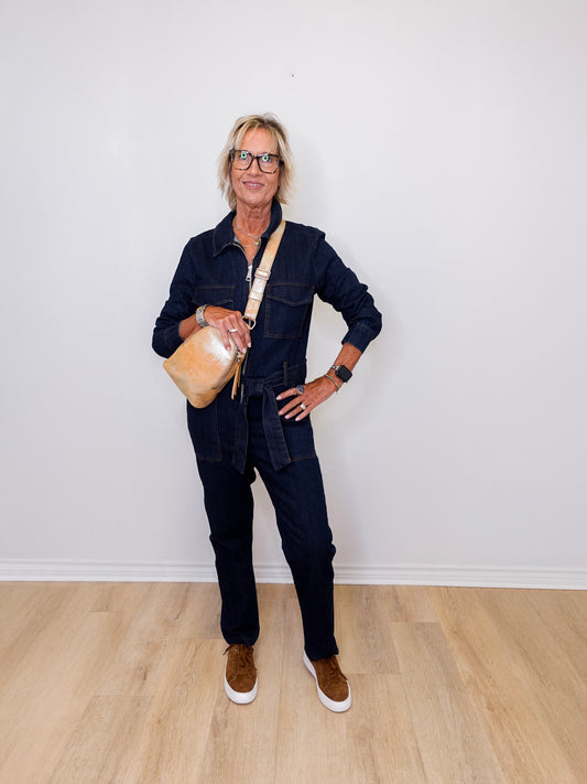 Person wearing a denim outfit with a beige bag against a white wall.