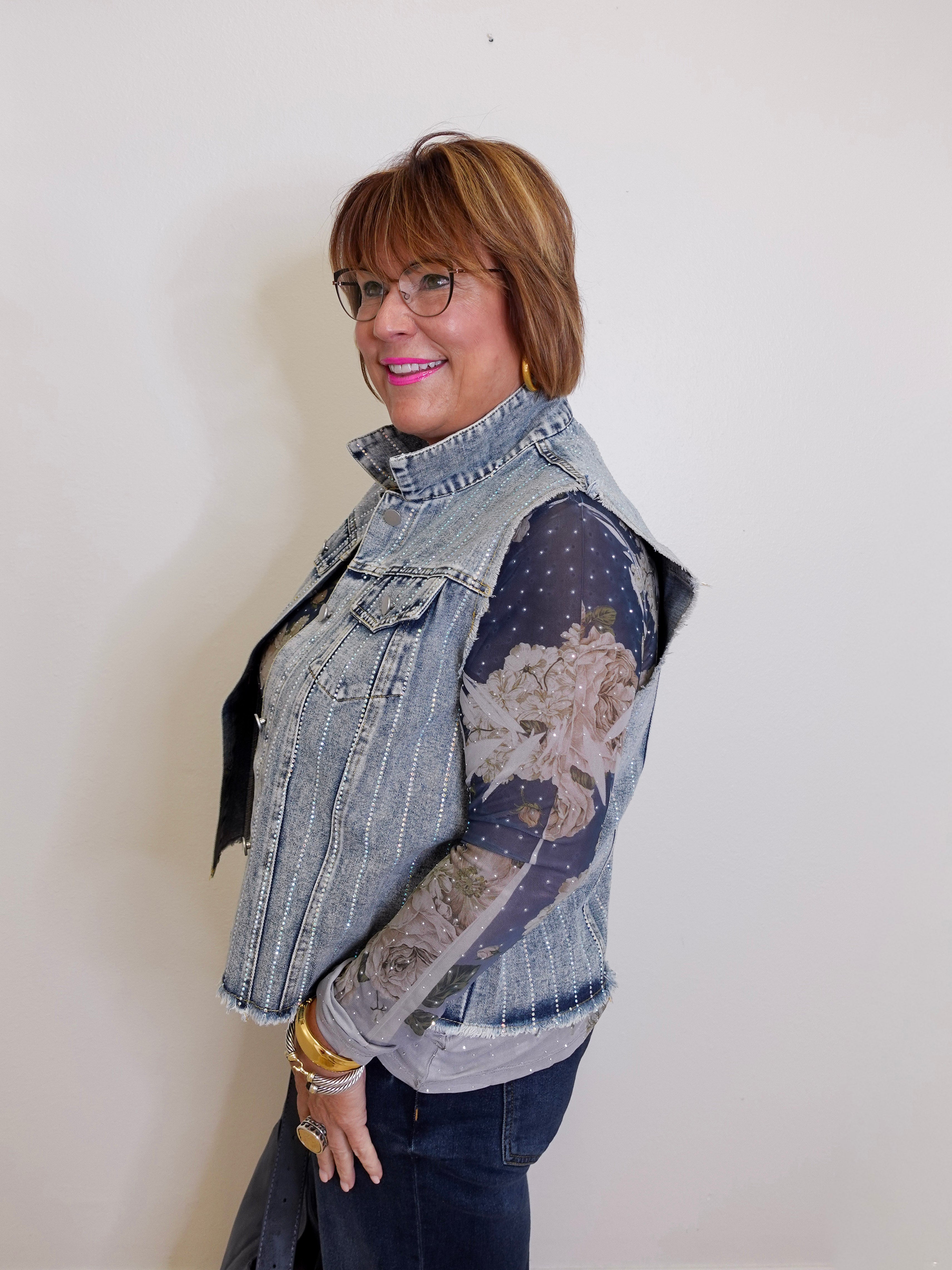 Woman wearing a denim vest over a patterned shirt against a plain background