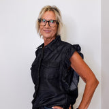 Woman wearing a black sleeveless shirt and glasses against a white background