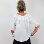 Person wearing a white blouse with yellow patterns and black shorts against a plain background