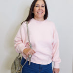 Woman wearing a pink sweater and blue jeans, holding a gray bag against a white background