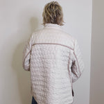 Person wearing a quilted jacket against a plain wall